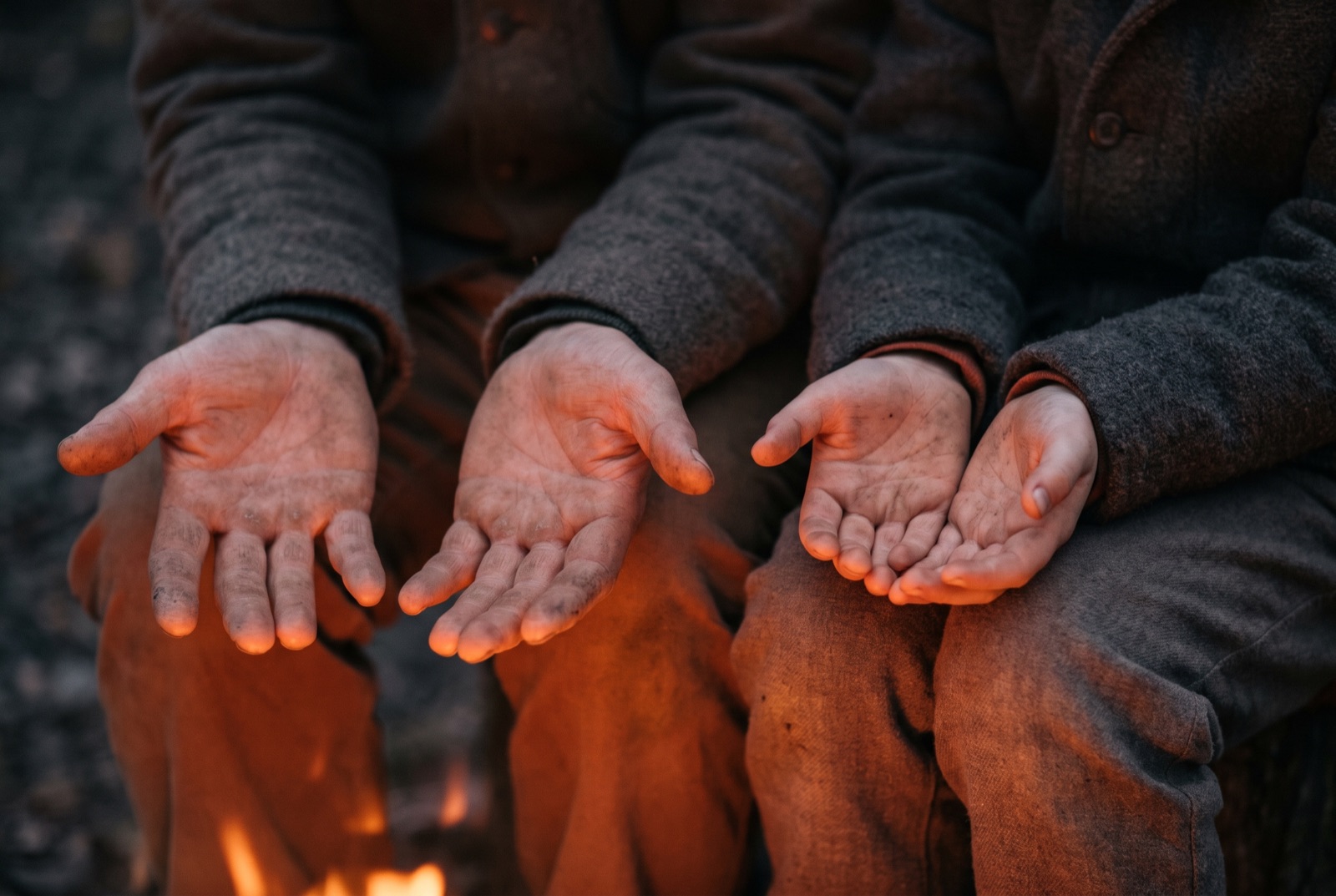 An adult's hands and a child's hands resting on knees in firelight, cropped at the forearm