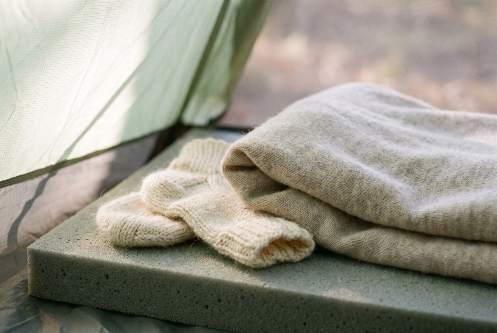 Tiny knitted wool socks and a folded merino base layer resting on a foam sleeping mat