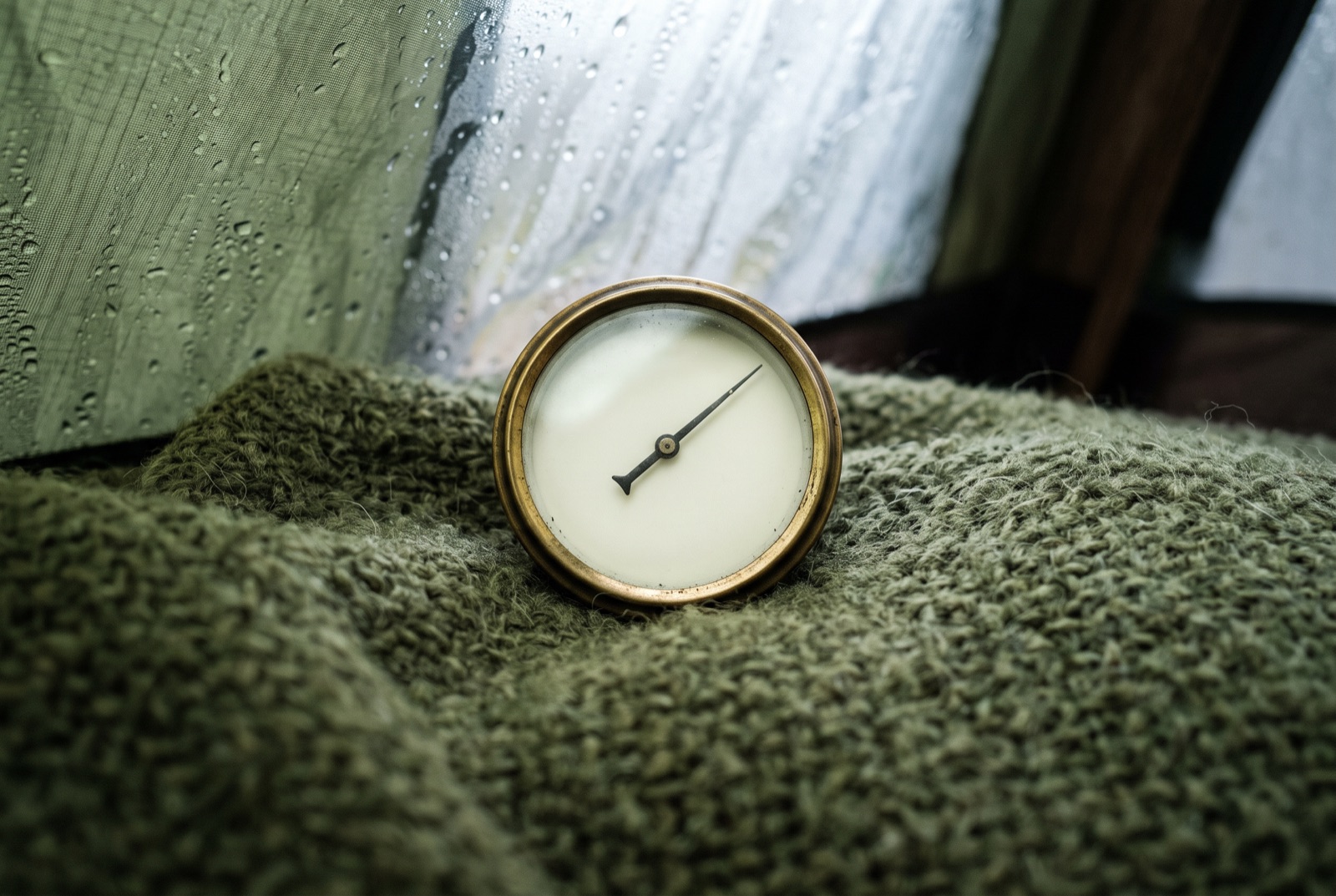 A small dial thermometer on a folded blanket inside a tent, with condensation on the fabric behind it