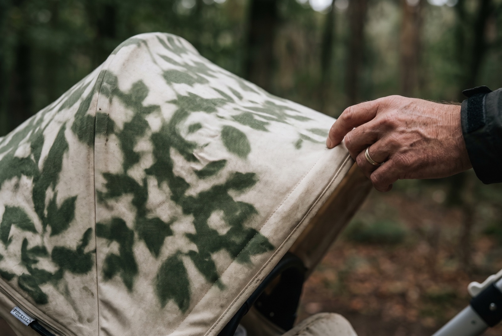 An adult's hand adjusting a pram canopy under dappled tree shade