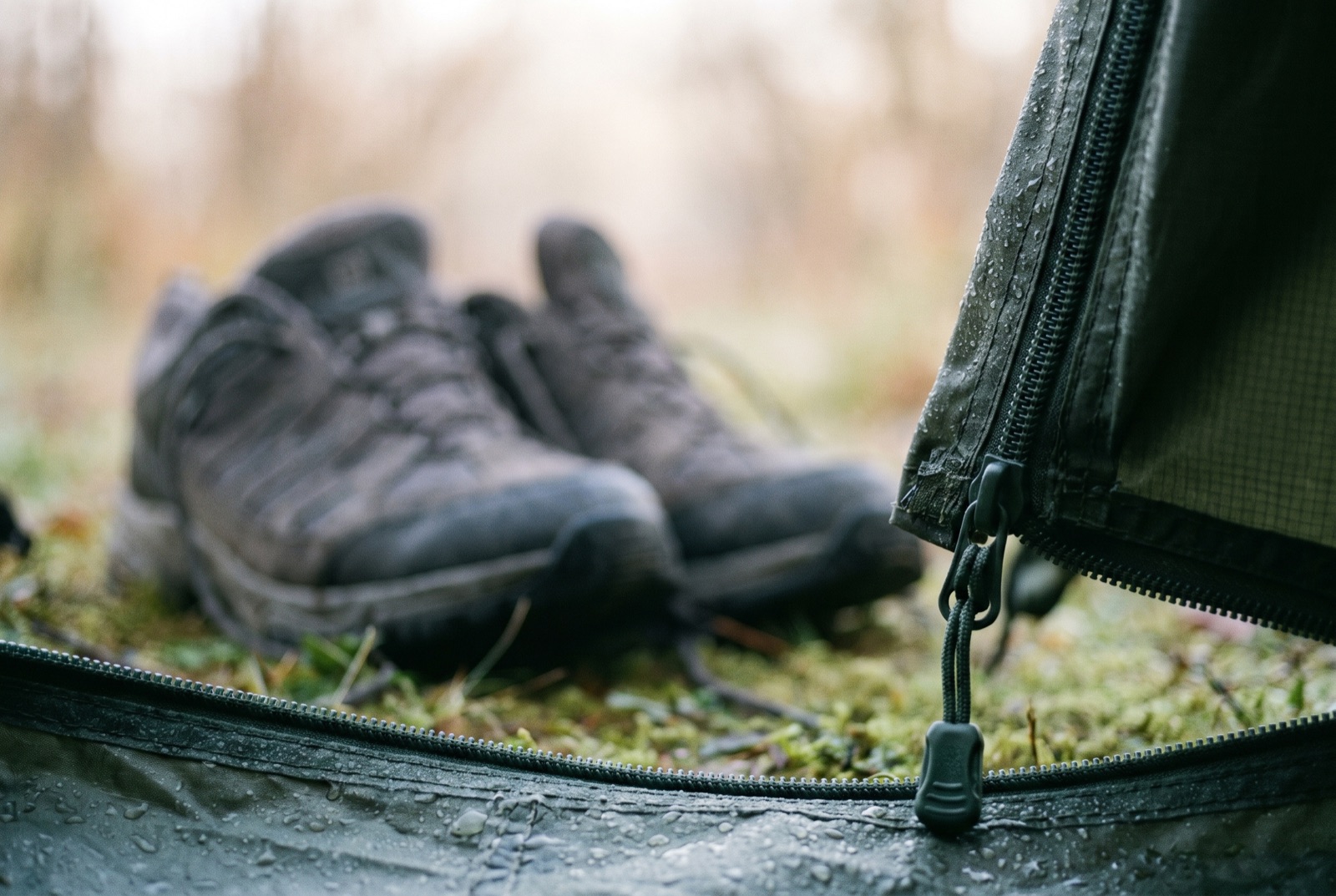 A half-open tent door with a pair of large trainers dropped inside on the groundsheet, dew on the fabric