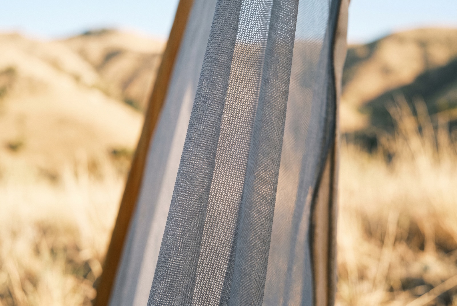 Close view of the mesh panel of a tent door with a bright, dry landscape blurred beyond it.