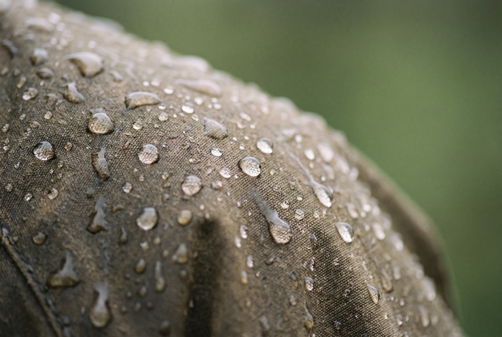 Rain beading on the shoulder of a waxed cotton jacket, droplets sitting on the surface of the fabric.