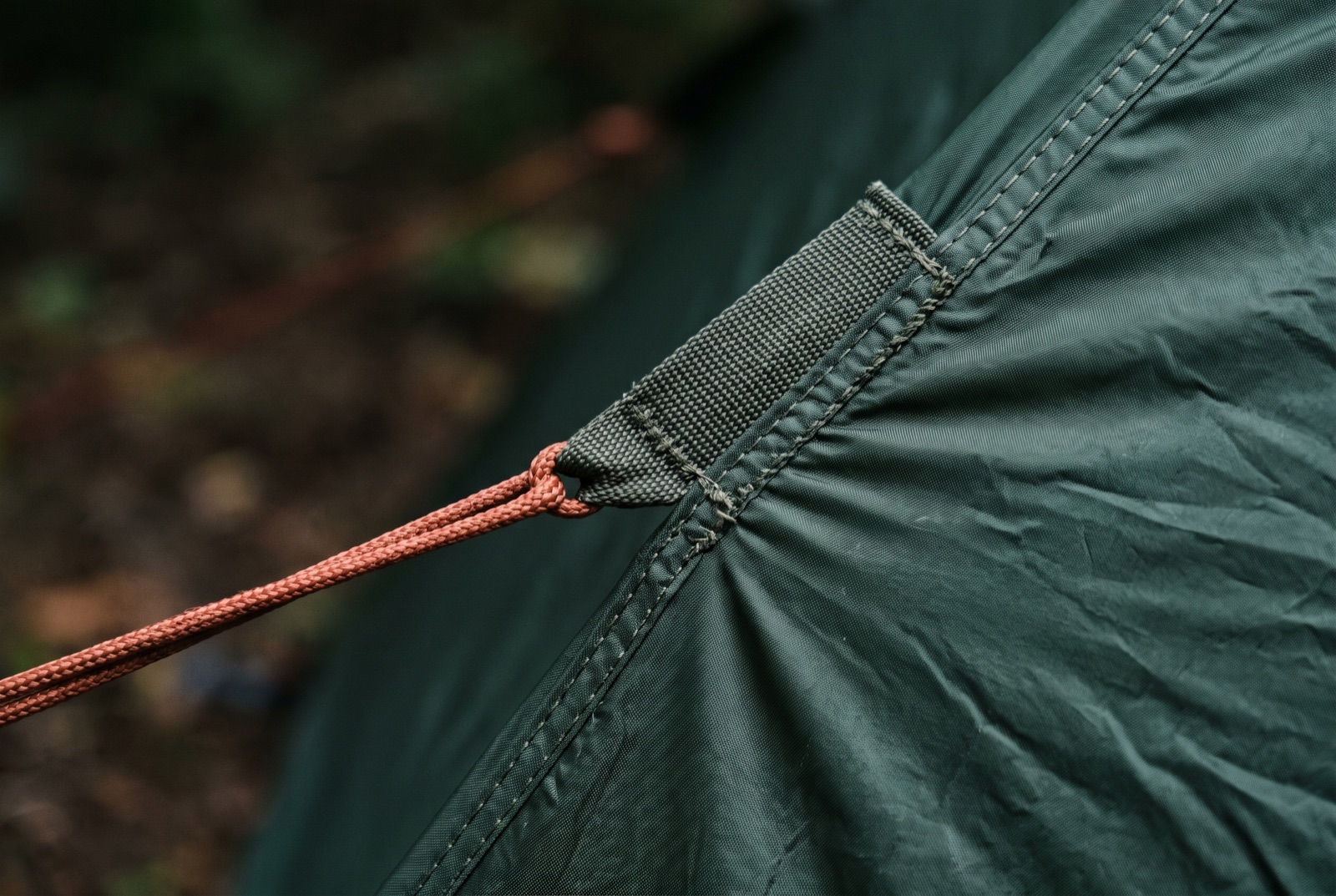 A guy line under tension at its attachment point on a flysheet, the fabric drawn into creases by the load.