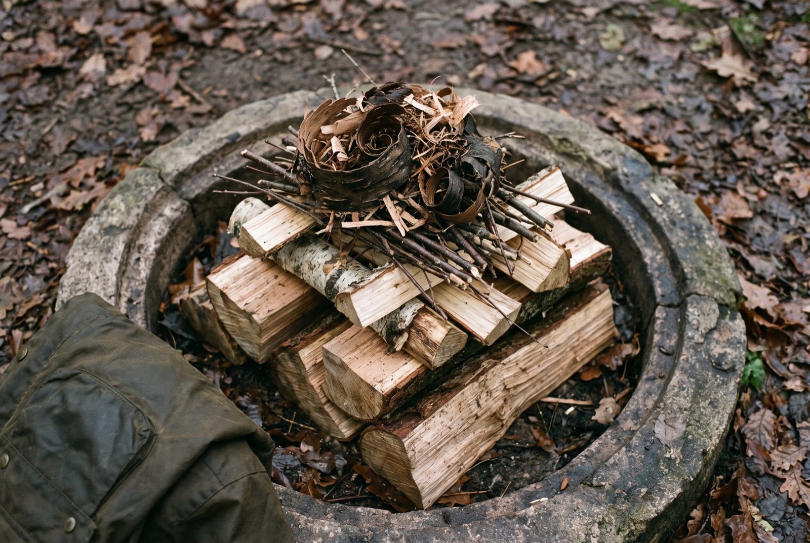 An unlit top-down fire lay inside a stone ring, with thick split logs at the base and progressively finer kindling stacked above.