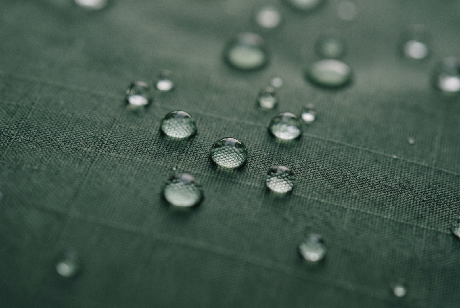 Extreme close-up of rain beading into tight spheres on the ripstop face fabric of a waterproof jacket