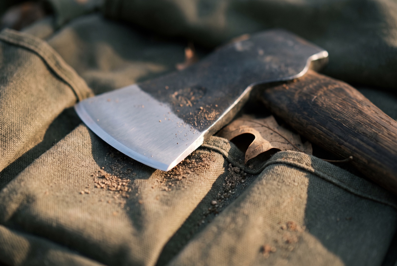 An unused hatchet lying in the bottom of a canvas bag, its blade still clean and unmarked.
