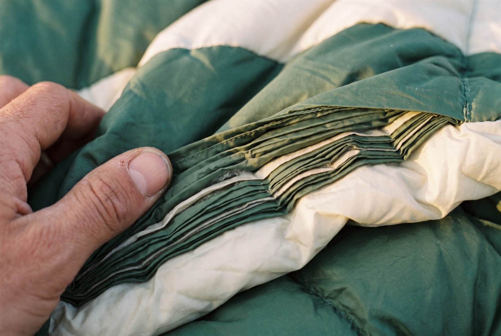A hand pressing into a down sleeping bag, flattening the baffles until the fill is almost no thickness at all